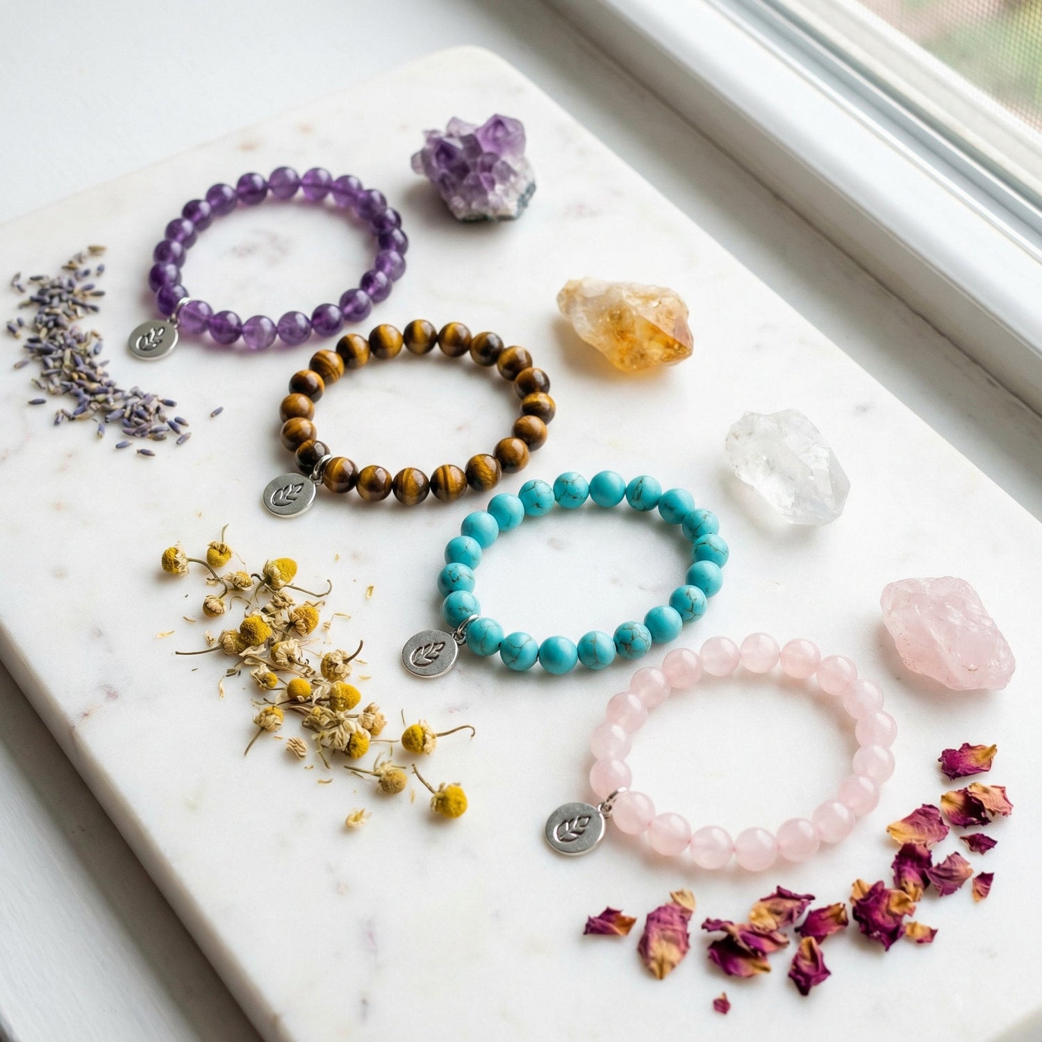 Flat lay de bracelets en pierres naturelles sur marbre blanc : améthyste violette, œil de tigre, turquoise et quartz rose avec cristaux