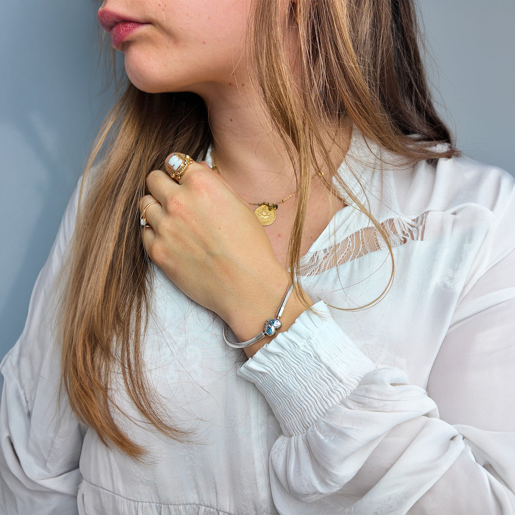 Bracelet fin argenté avec charms papillon et cœur, porté sur poignet féminin en chemise blanche.
