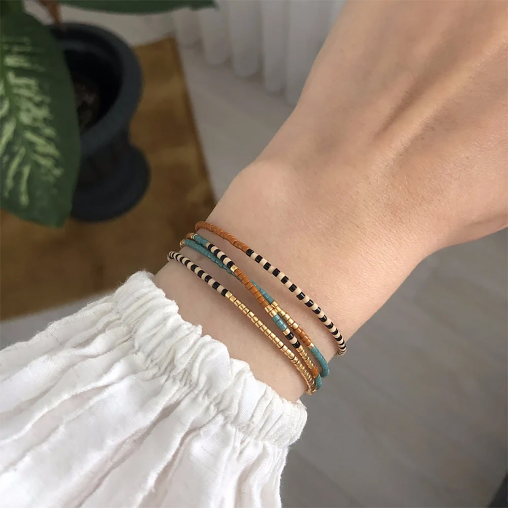 Bracelet à perles Miyuki turquoise, or et brun, cordon ajustable, style bohème chic, porté au poignet.