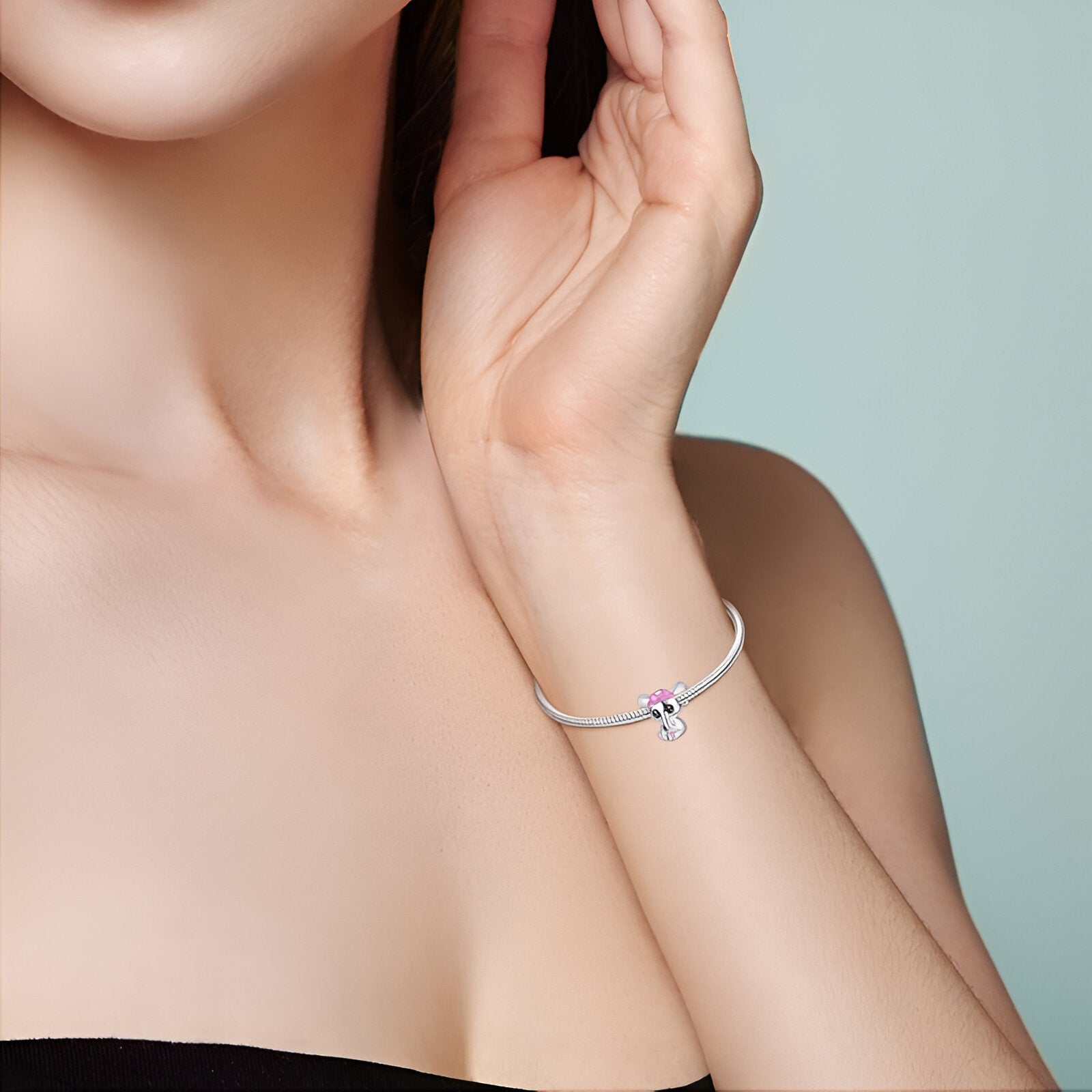 Bracelet argenté fin avec charm éléphanteau en métal et détail rose sur poignet féminin.