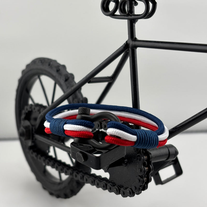 Bracelet cordon bleu blanc rouge avec mousqueton en acier inoxydable posé sur pédale de vélo noir miniature.