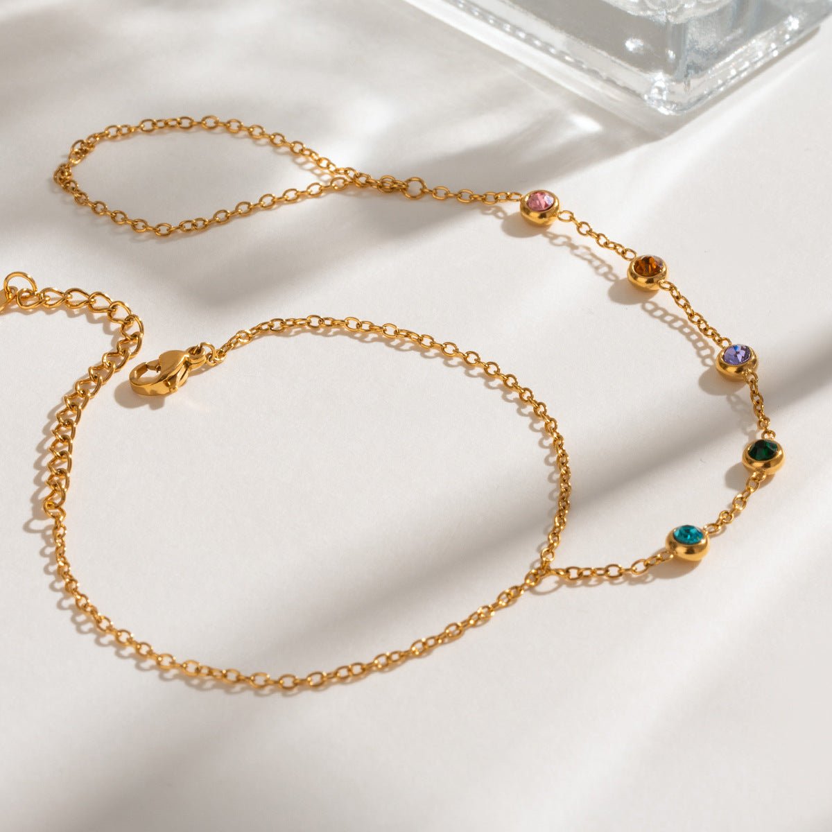 Chaîne de main fine dorée avec pierres de zirconium multicolores brillantes, design délicat et élégant.