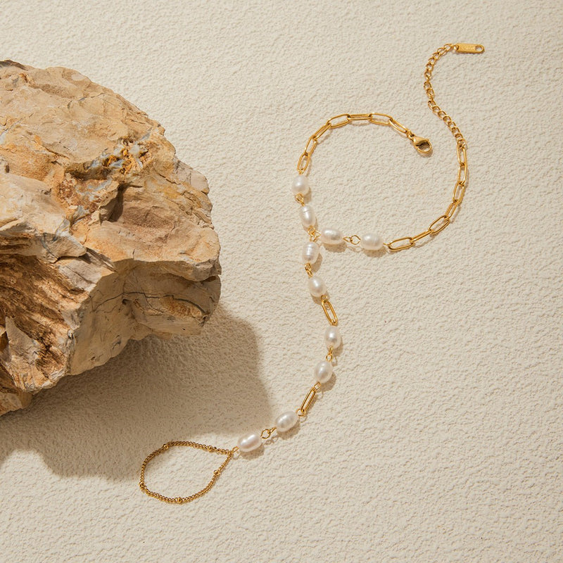 Bracelet de main en acier inoxydable doré avec perles blanches ovales et chaîne fine élégante.