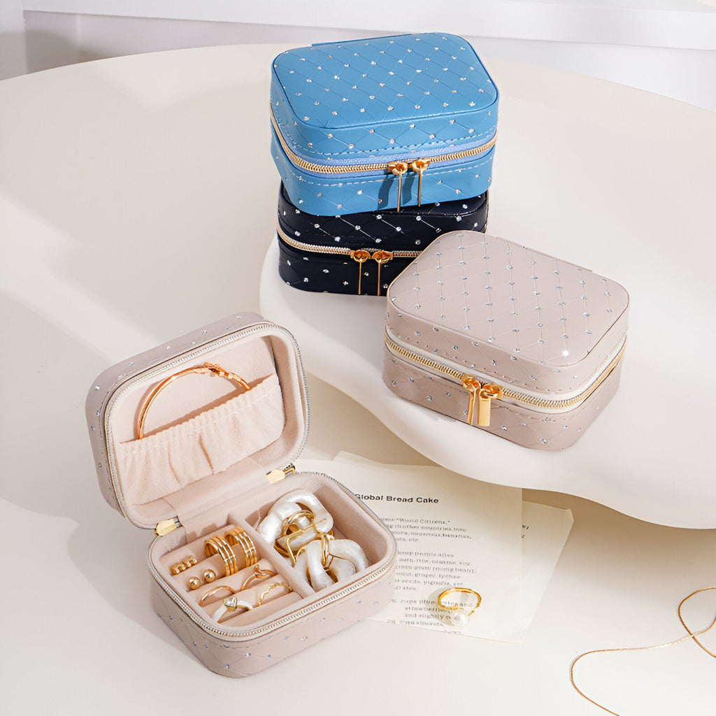 Boîtes à bijoux nomades bleue, noire et beige en tissu à strass avec fermeture éclair dorée.