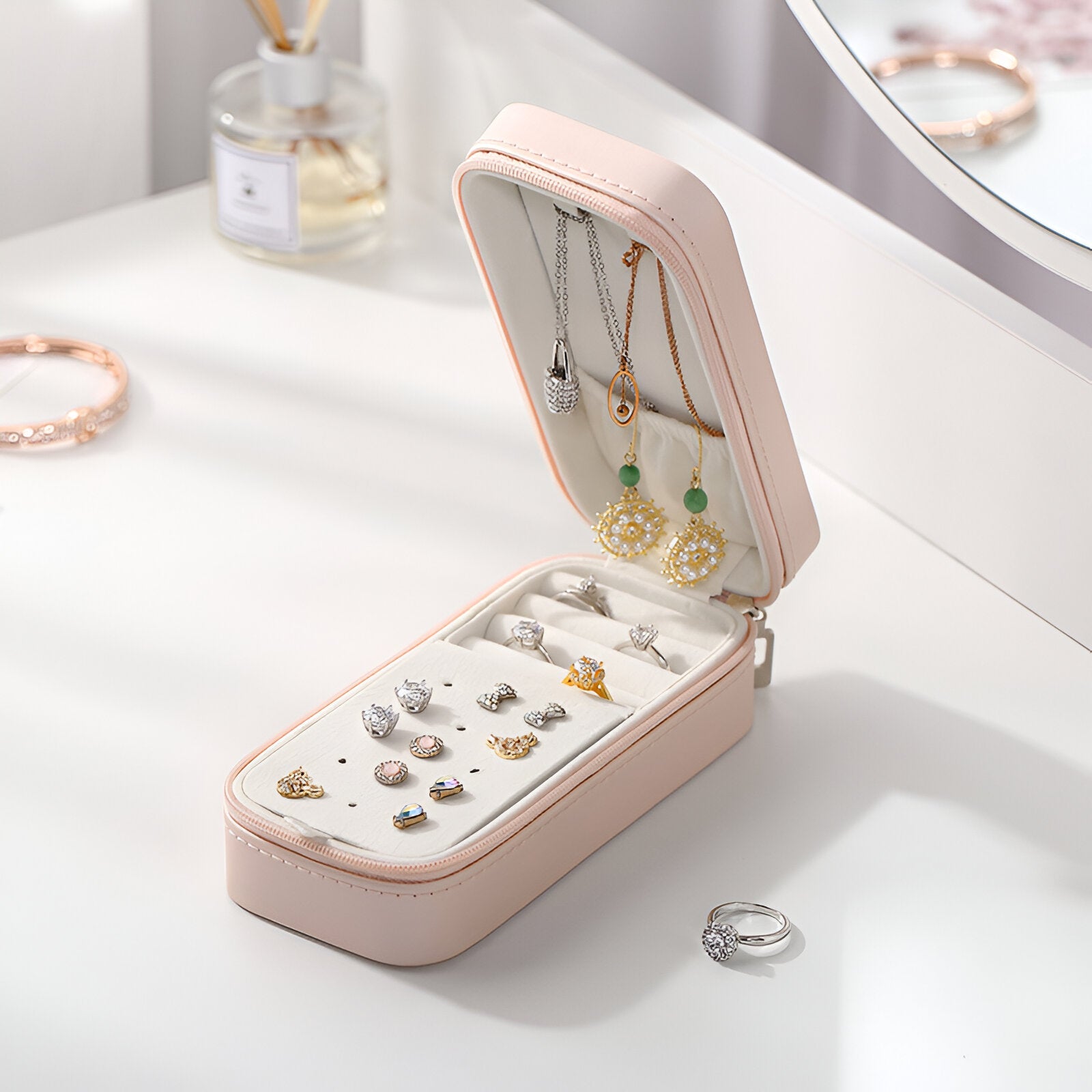 Boîte à bijoux nomade allongée rose avec compartiments pour bagues, boucles d'oreilles et colliers suspendus.