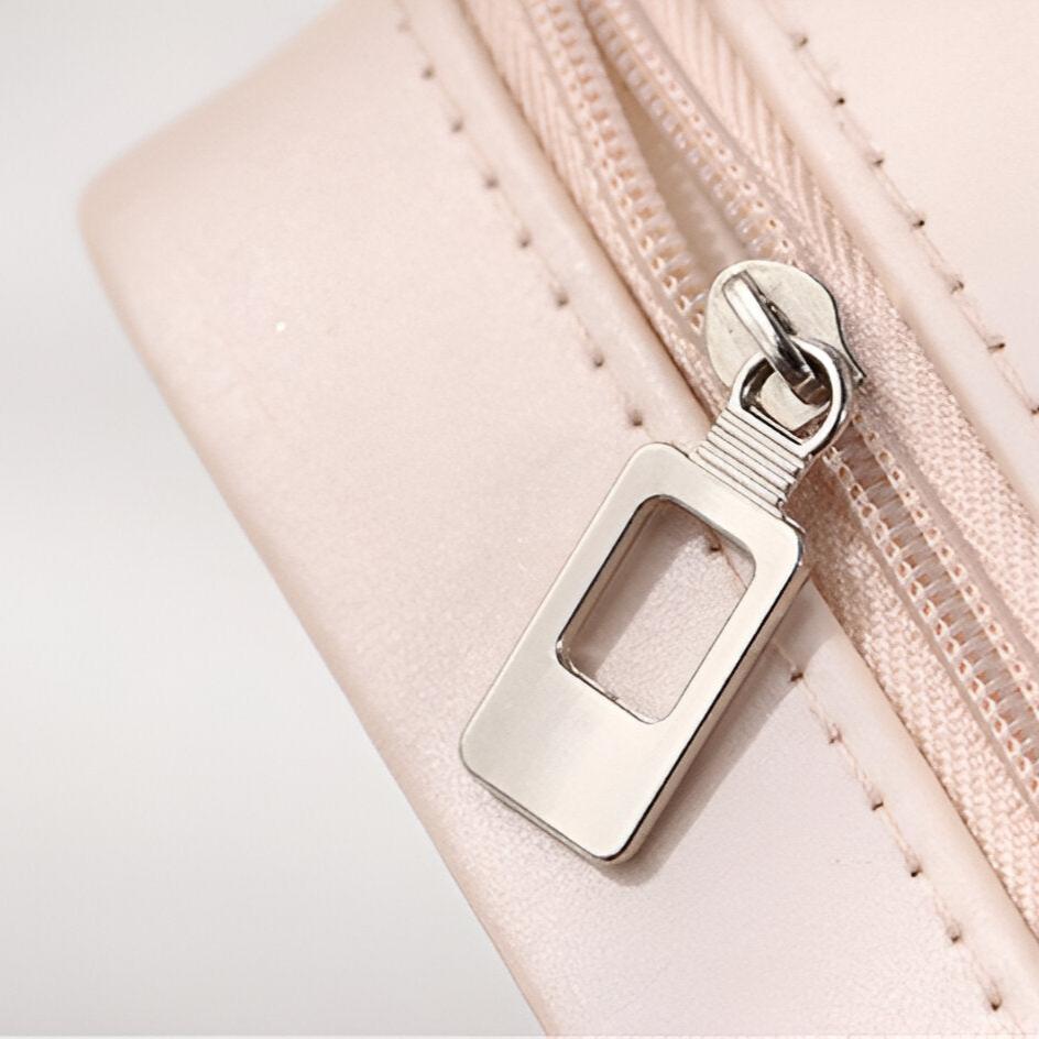 Détail de la fermeture éclair argentée sur boîte à bijoux nomade rose pâle en cuir lisse.