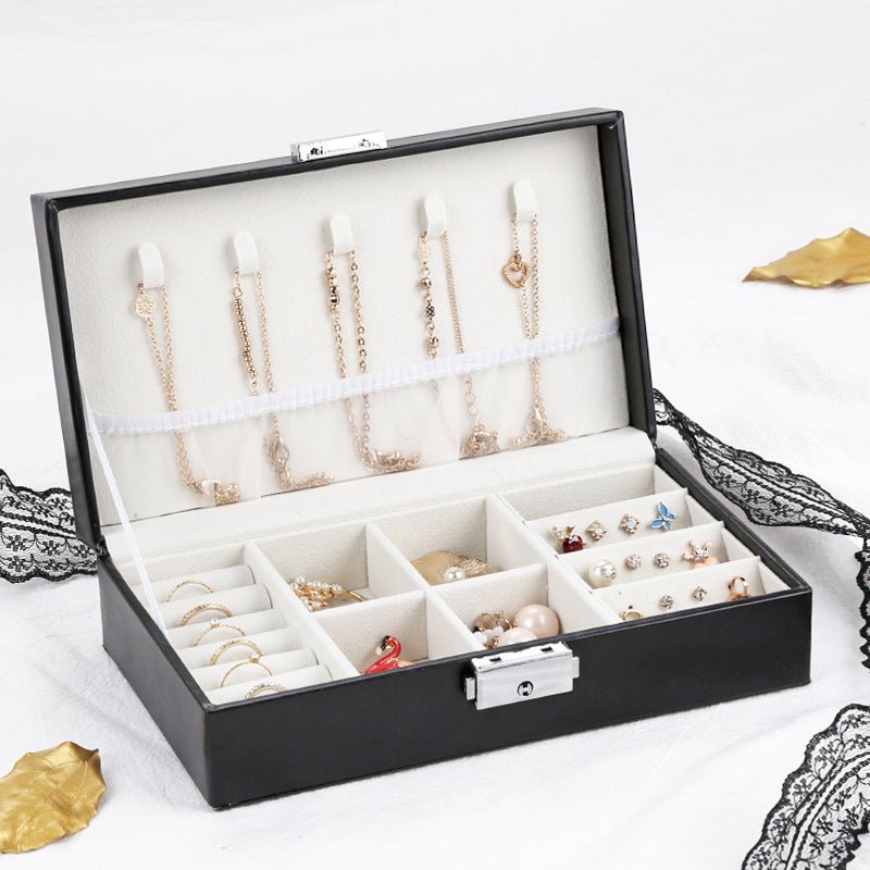 Boîte à bijoux noire ouverte avec rangements divisés pour bagues, boucles d'oreilles et colliers, intérieur velours beige.