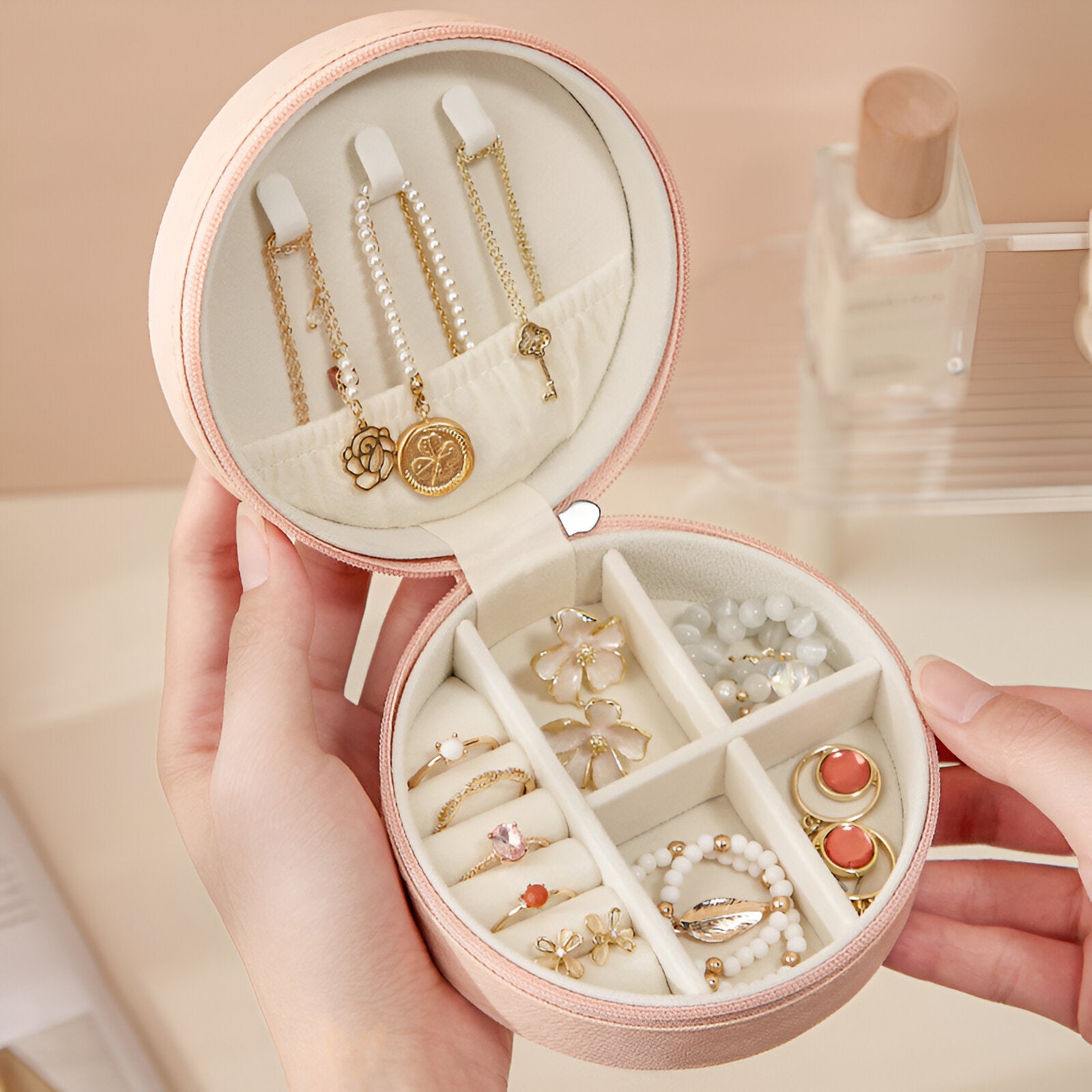 Boîte à bijoux ronde rose avec compartiments, bijoux dorés et perles organisés à l'intérieur.