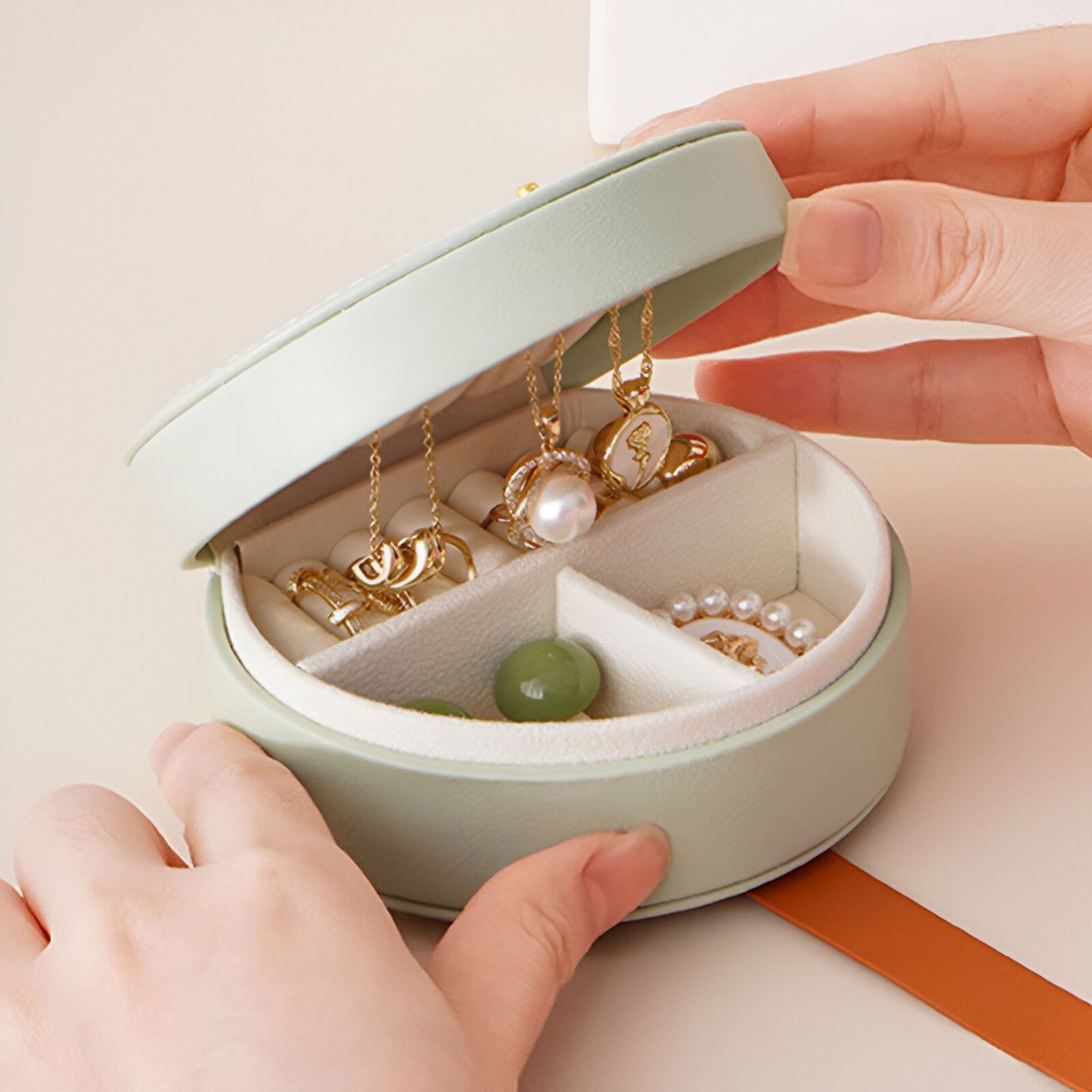 Boîte à bijoux ronde verte avec compartiments et garnie de bijoux dorés et perles.
