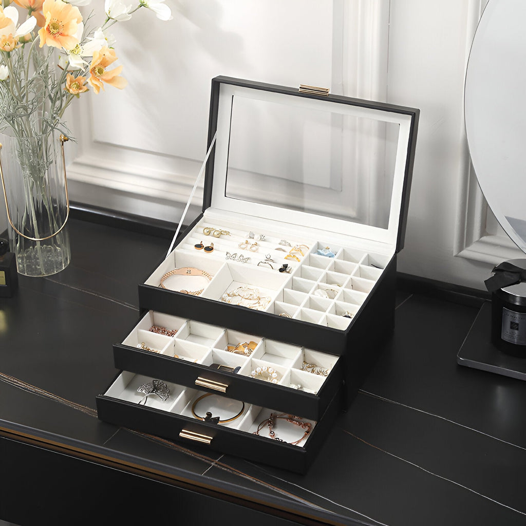 Boîte à bijoux nomade noire grand format avec tiroirs multiples et compartiments variés, couvercle en verre transparent.