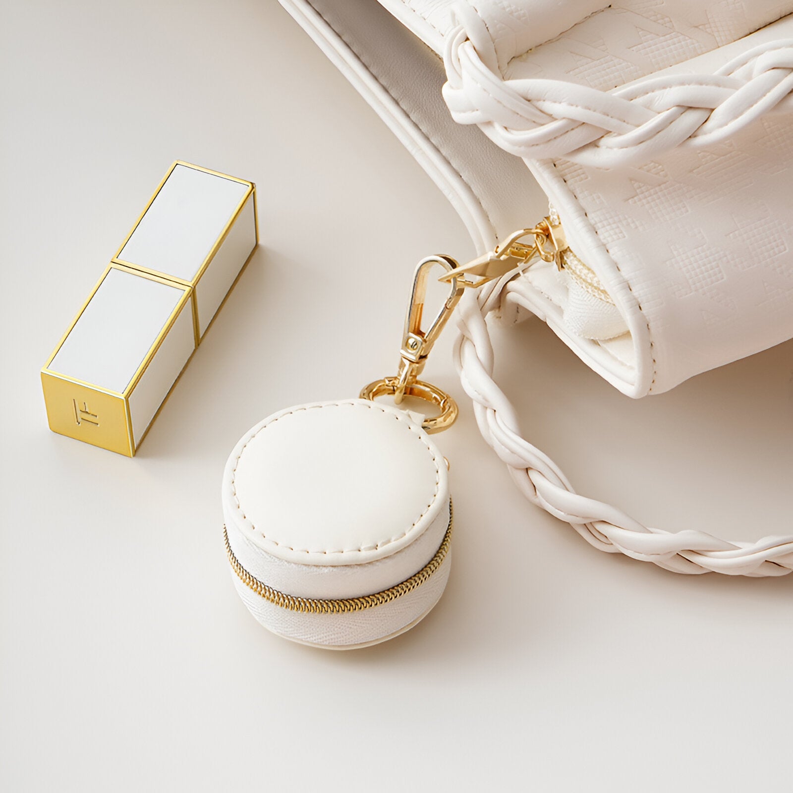 Boîte à bijoux nomade ronde mini blanche avec fermeture dorée accrochée à un sac blanc tressé.