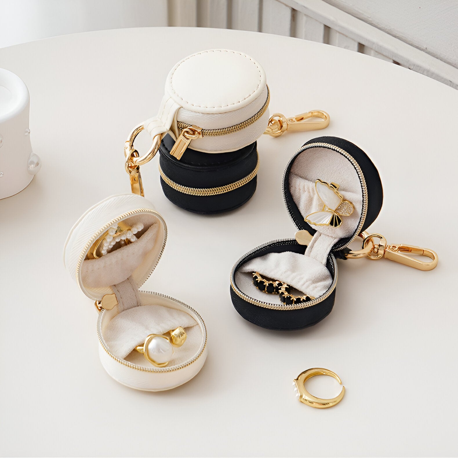 Boîtes à bijoux nomades mini format en cuir blanc et noir avec doublure beige, accessoires dorés, fermeture zippée.