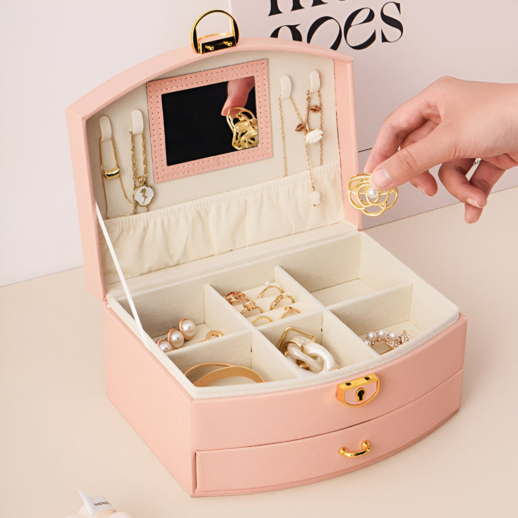 Boîte à bijoux rose nomade en cuir avec miroir intégré, plusieurs compartiments et porte-bagues.