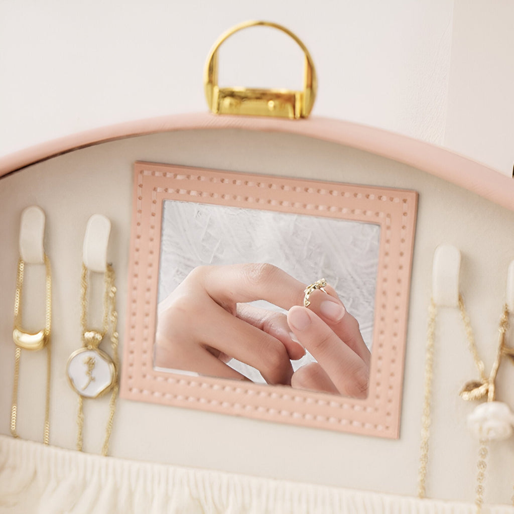 Boîte à bijoux rose avec miroir carré intégré et plusieurs compartiments pour chaînes et montres.