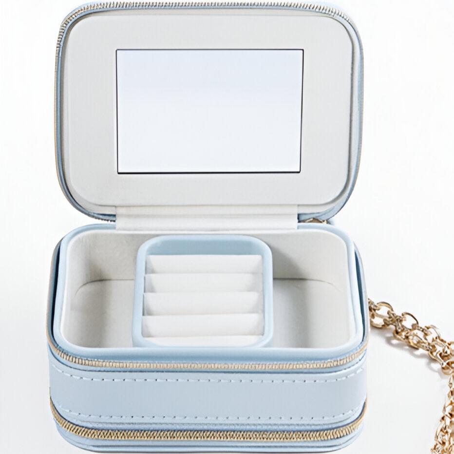 Boîte à bijoux nomade bleue en cuir, intérieur compartimenté avec miroir et fermoir chaîne dorée.