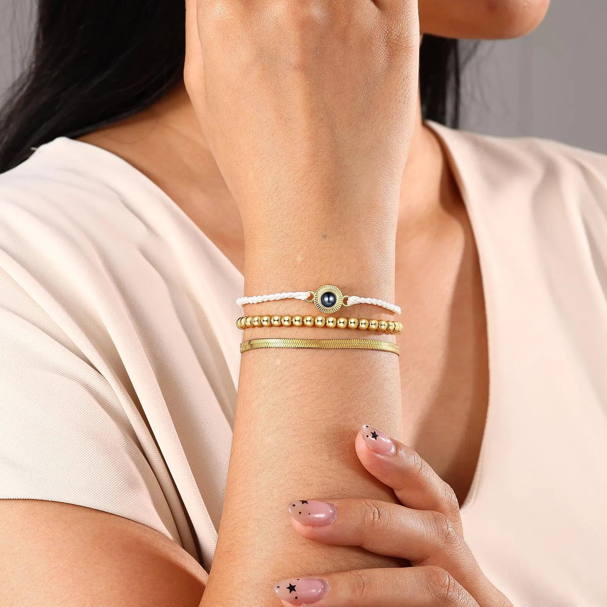 Bracelet à cordon tressé beige avec trois perles dorées et médaille acier inoxydable gravée, style élégant et moderne.