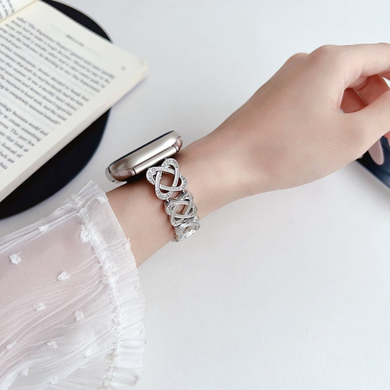 Pulseira para Apple Watch em metal prateado com malhas entrelaçadas, motivo de nó infinito cravejado de zircónias, fecho de encaixe ajustável, modelo Zergone