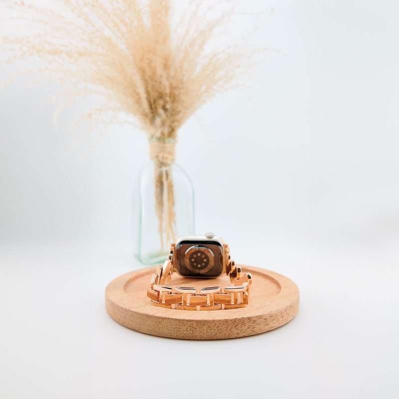 Bracelet spirale en acier rose doré pour Apple Watch, design moderne et élégant, posé sur socle en bois clair.