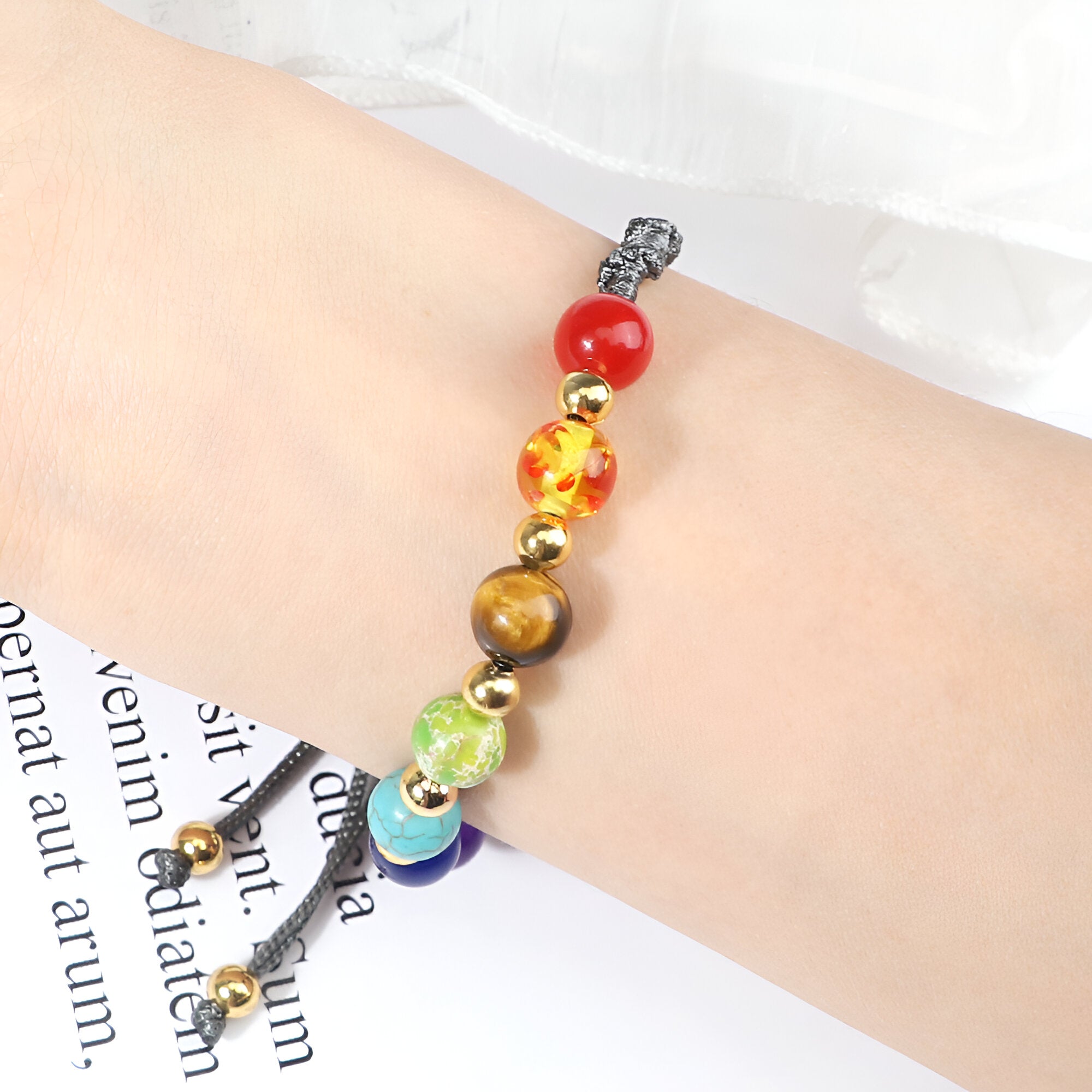 Bracelet aux 7 chakras en pierres naturelles multicolores et corde noire ajustable sur poignet clair.