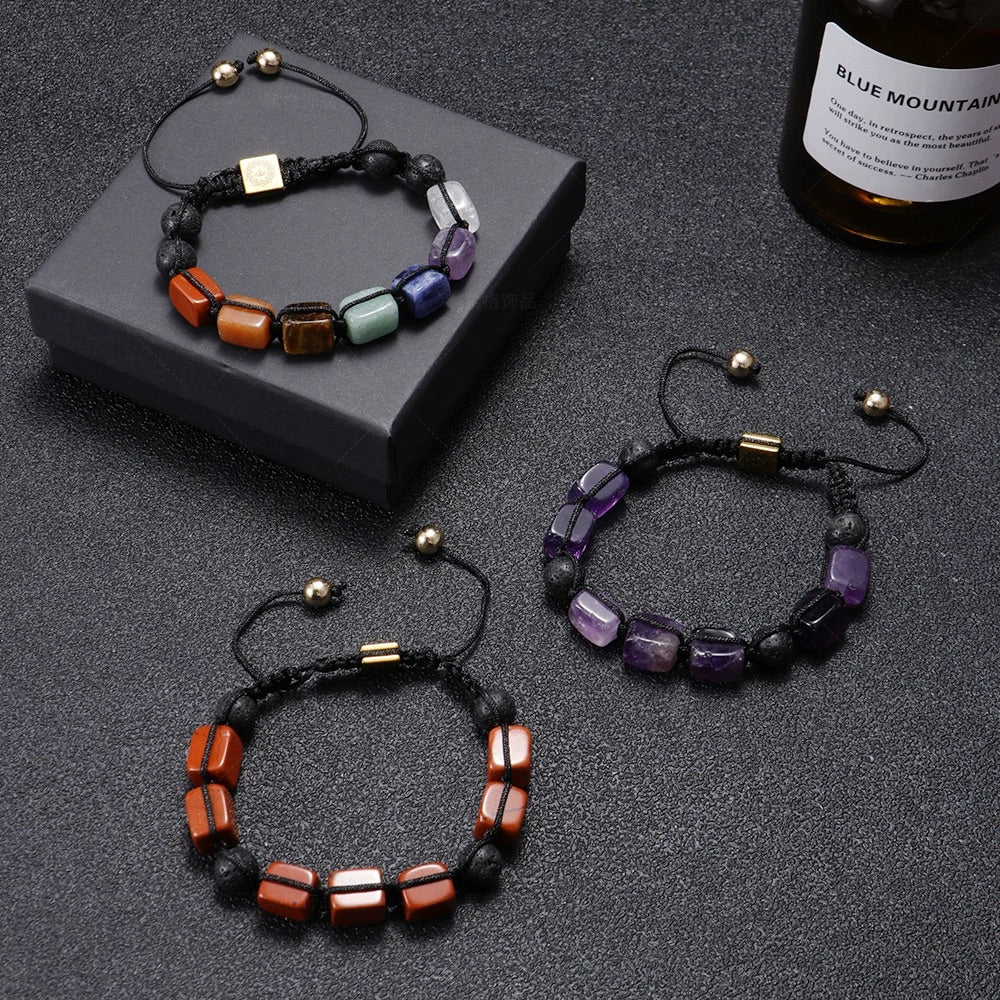 Bracelet en corde noire avec pierres naturelles rectangulaires rouges et détails métalliques dorés sur boîte grise .