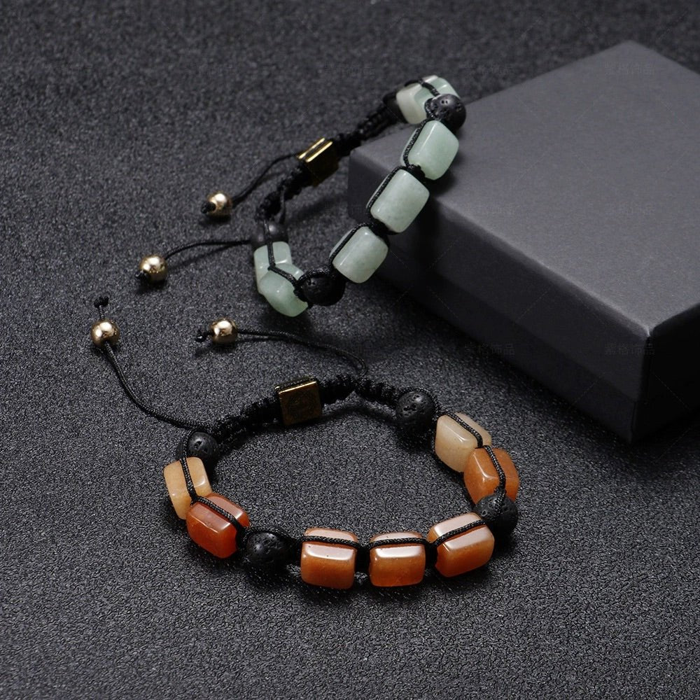 Bracelet en corde noire avec pierres carrées rouges et noires, fermoir coulissant doré et noir, posé sur boîte grise, avec.