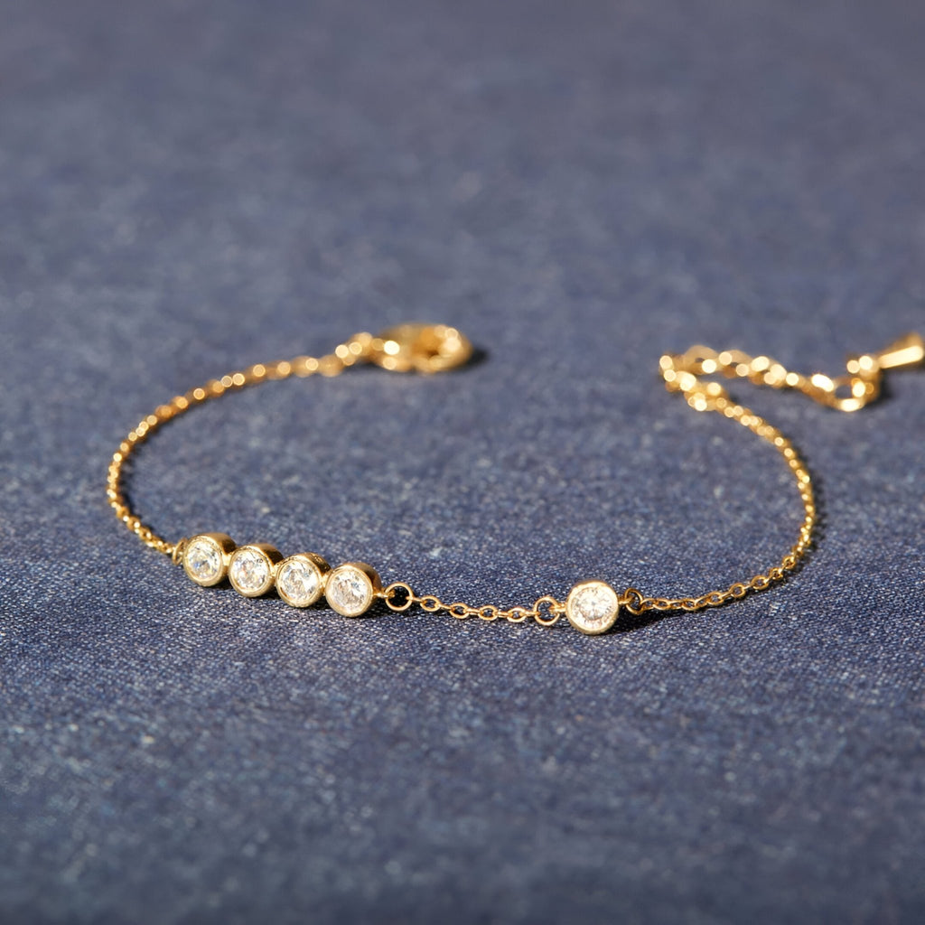 Bracelet fin en or avec cinq pierres scintillantes rondes sur une chaîne délicate.