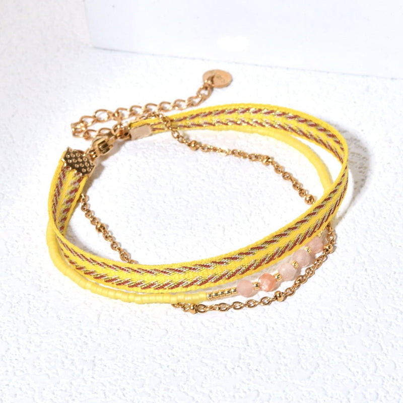 Bracelet bohème multirangs jaune avec perles fantaisie roses, ruban rayé et chaîne dorée fine, fermoir mousqueton.