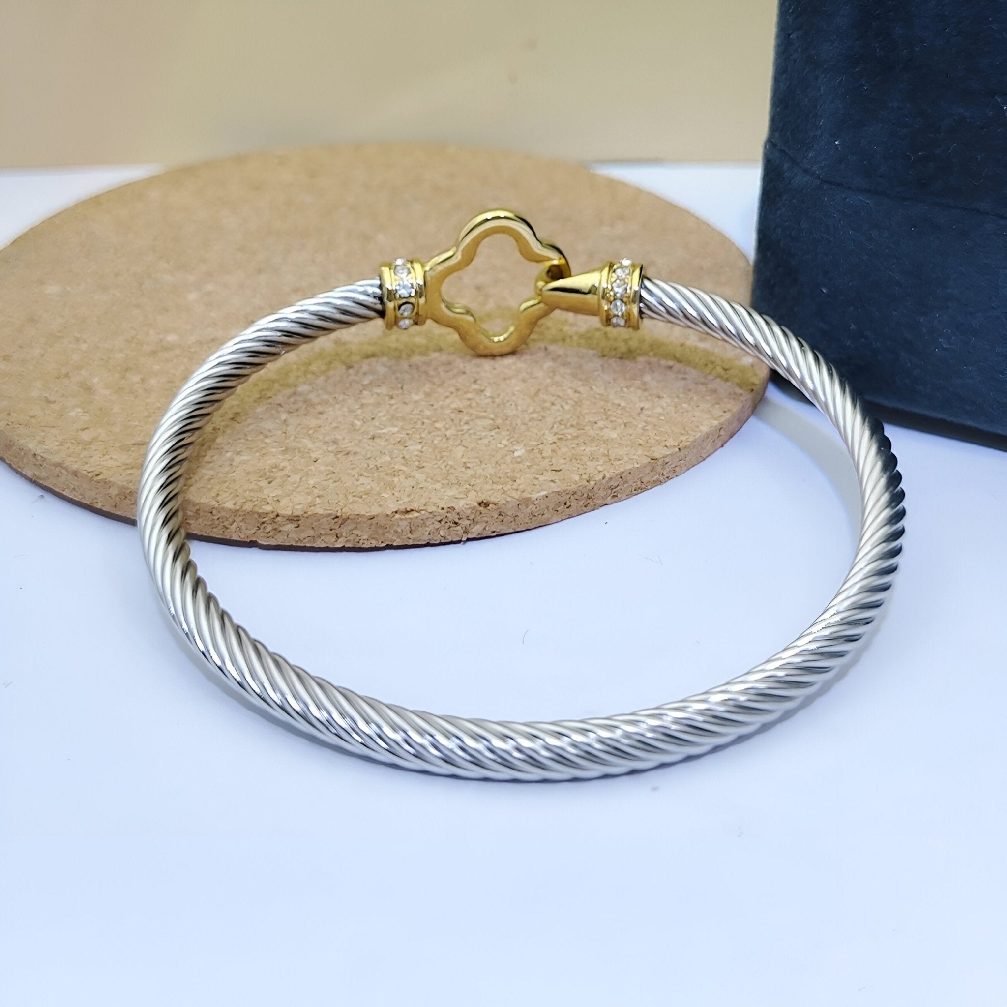 Bracelet câble argenté en acier inoxydable avec fermoir doré en forme de trèfle.