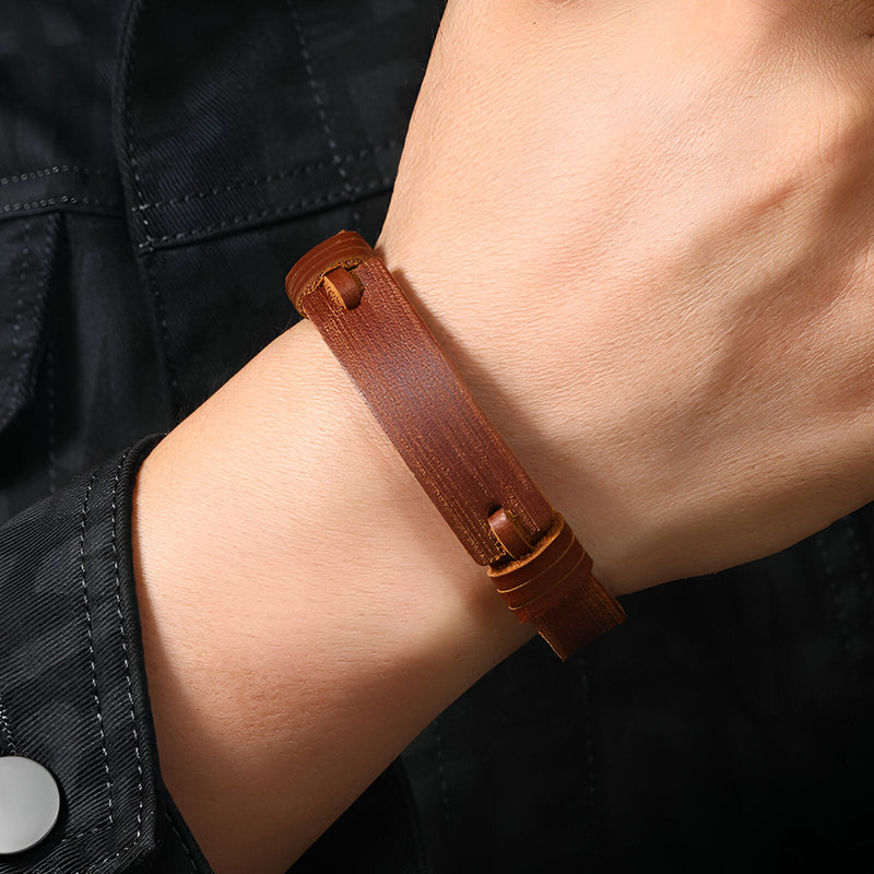 Bracelet en cuir marron effet vintage avec fermeture bouton-pression en métal sur poignet masculin.