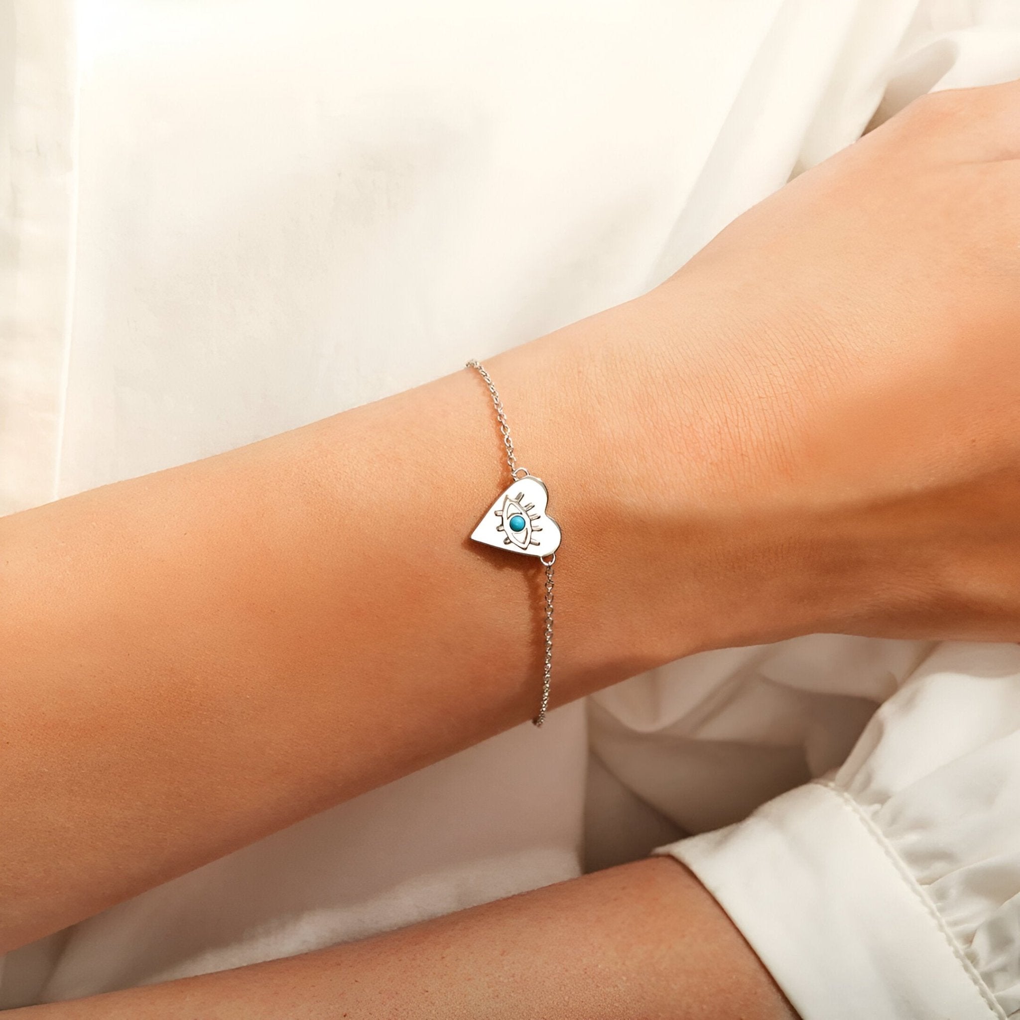 Bracelet en argent sterling à chaîne fine avec pendentif cœur orné d'un œil bleu sur poignet féminin.