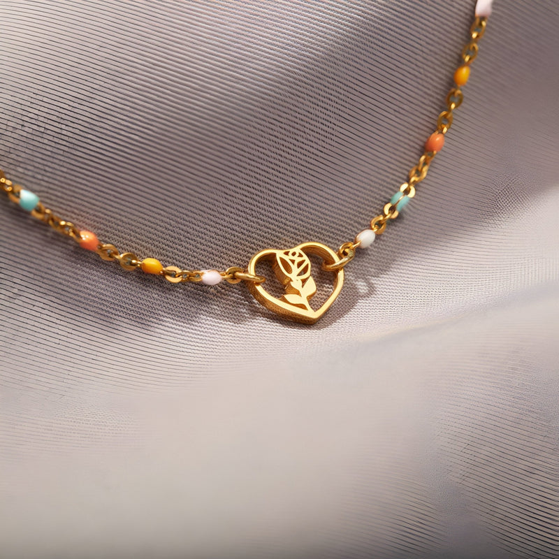 Bracelet en or avec pendentif cœur ajouré et rose stylisée, chaîne fine ornée de perles colorées.