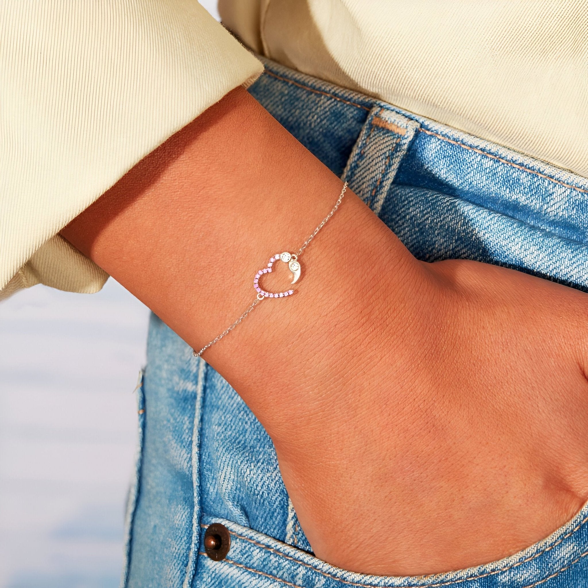 Bracelet fin en argent sterling avec pendentif cœur rosé ajouré porté au poignet féminin.