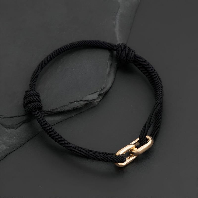 Bracelet cordon noir avec maillons croisés dorés, style moderne et minimaliste.