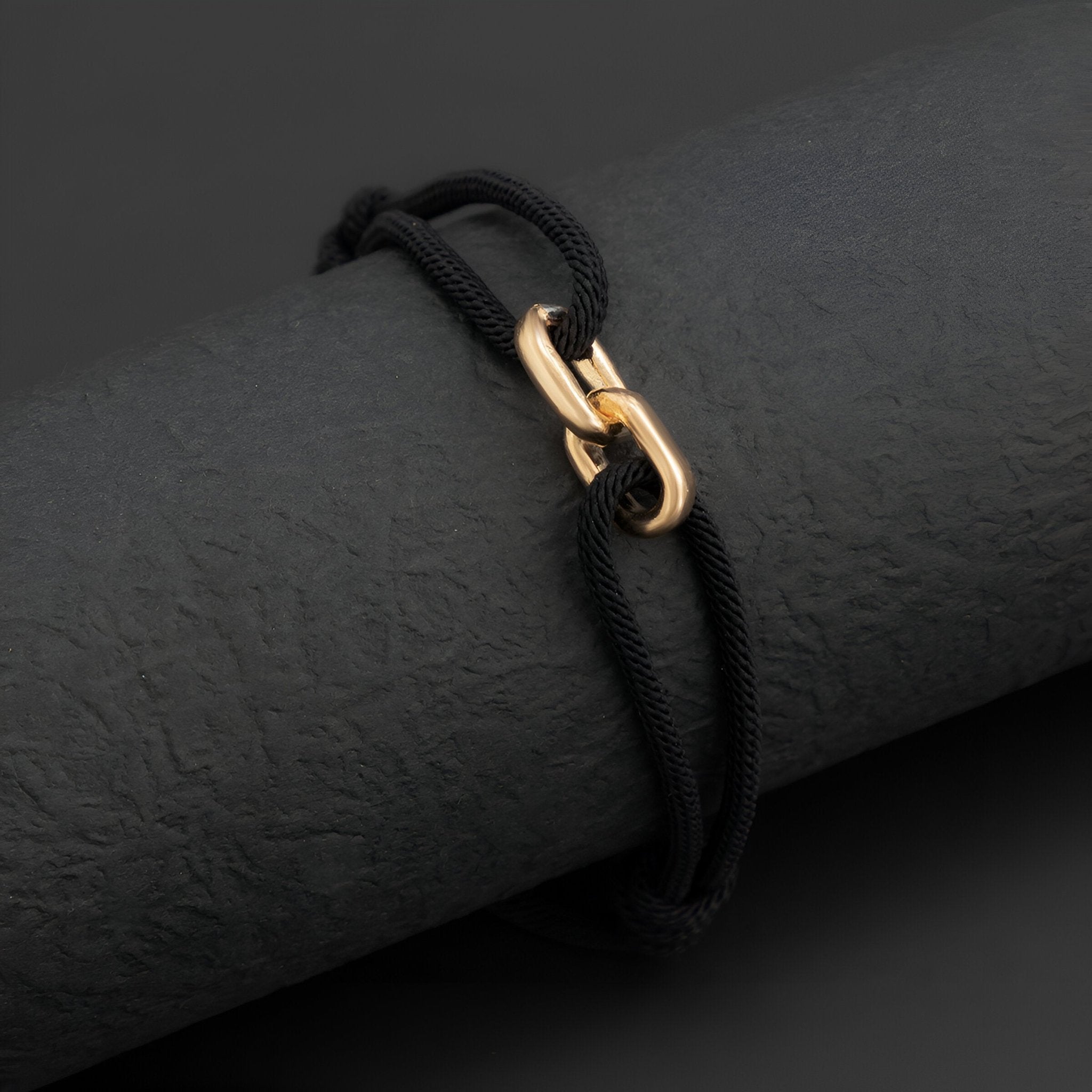 Bracelet cordon noir avec maillons croisés en métal doré éclatant.