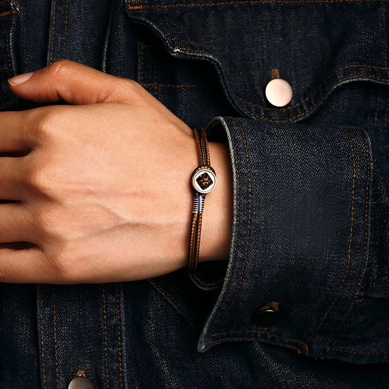 Bracelet cordon marron avec pendentif en argent sterling élégant porté sur poignet homme en veste en jean bleue.