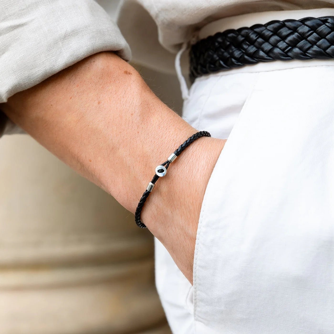 Bracelet cordon noir tressé avec petit médaillon argenté minimaliste au poignet homme.