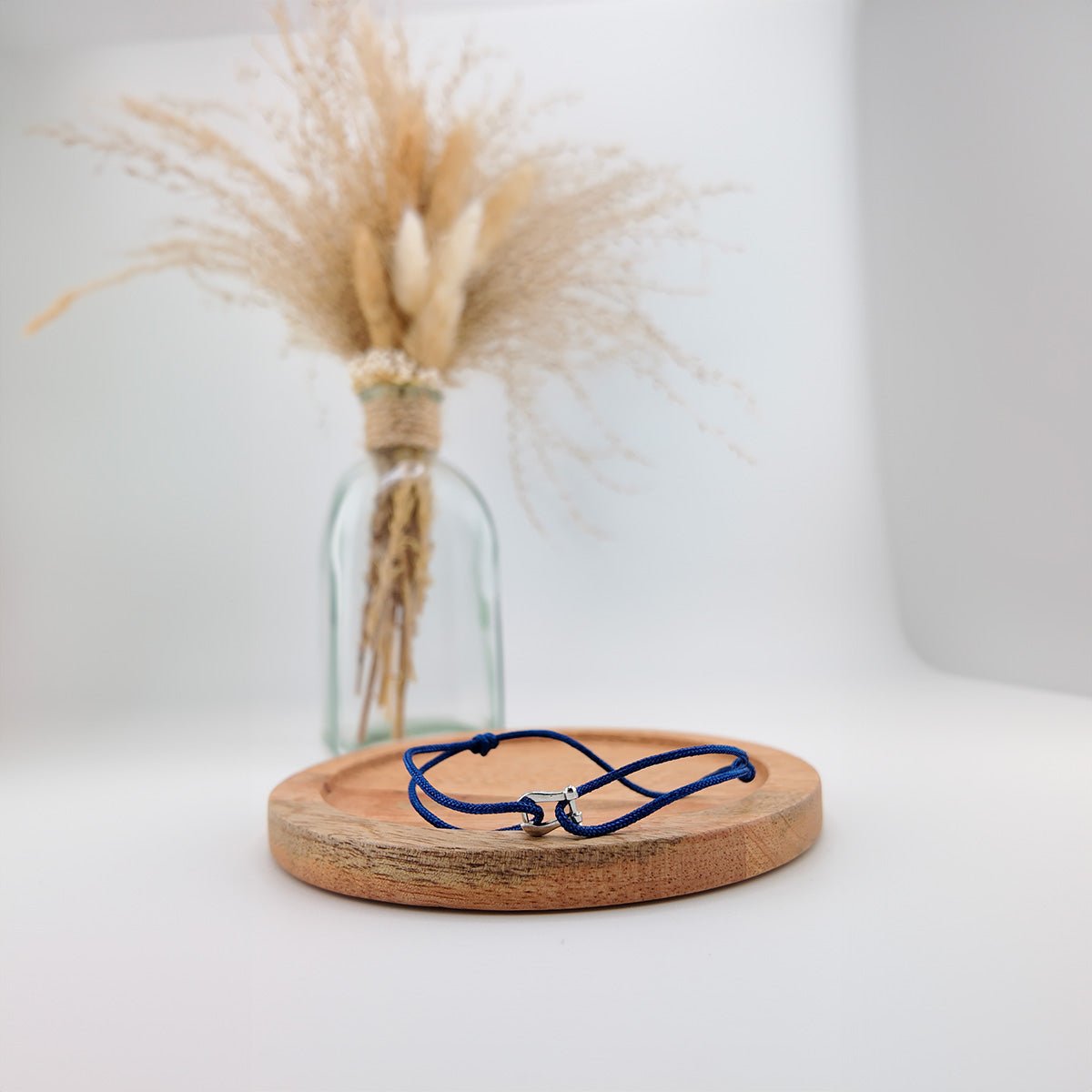 Bracelet cordon bleu marine avec pendentif en forme de fer à cheval en acier inoxydable sur plateau rond en bois clair.