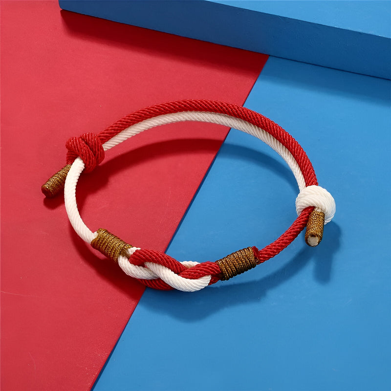 Bracelet cordon bicolore rouge et blanc avec nœud central et finitions dorées.