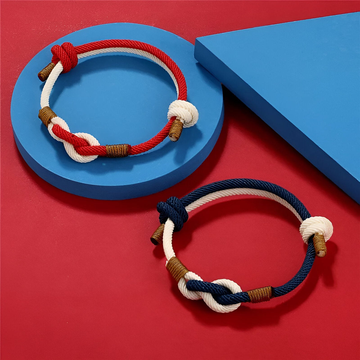 Bracelet cordon bi-colore rouge et beige avec nœud central blanc et détails métalliques dorés .