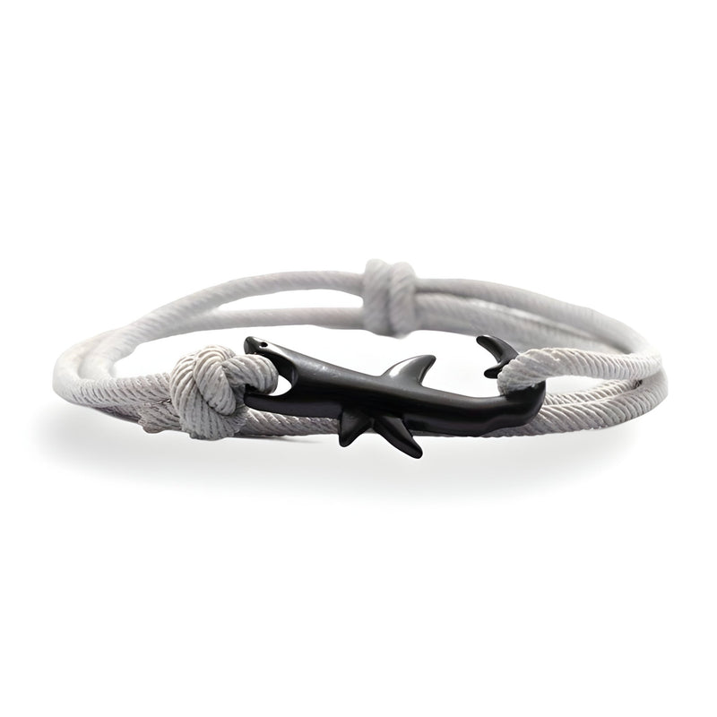 Bracelet cordon blanc avec pendentif requin noir stylisé et fermoir noeud coulissant.