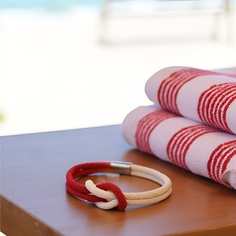 Bracelet cordon bi-couleur rouge et blanc avec nœud et fermoir argenté sur table en bois.