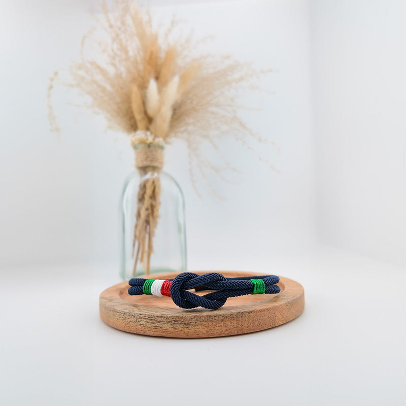 Bracelet cordon bleu marine avec nœud marin et bandes aux couleurs du drapeau italien sur support en bois clair.