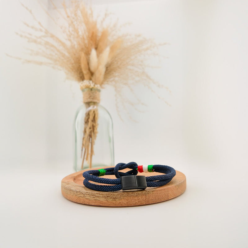 Bracelet cordon bleu marine avec nœud marin et détails vert, blanc, rouge rappelant le drapeau italien, fermoir noir mat.