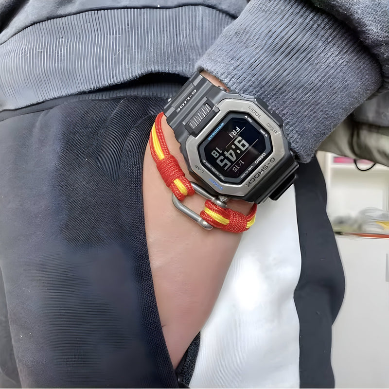 Bracelet cordon rouge et jaune avec manille acier inoxydable porté avec montre digitale noire et grise.