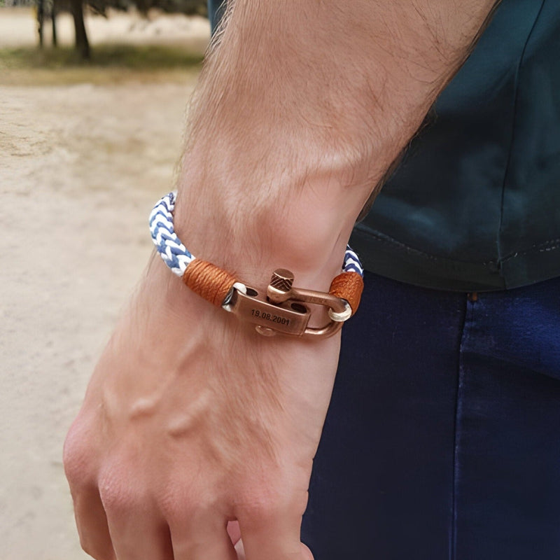 Bracelet cordon bleu et blanc avec fermoir mousqueton ancien en métal cuivré et détails en cuir marron sur poignet masculin.