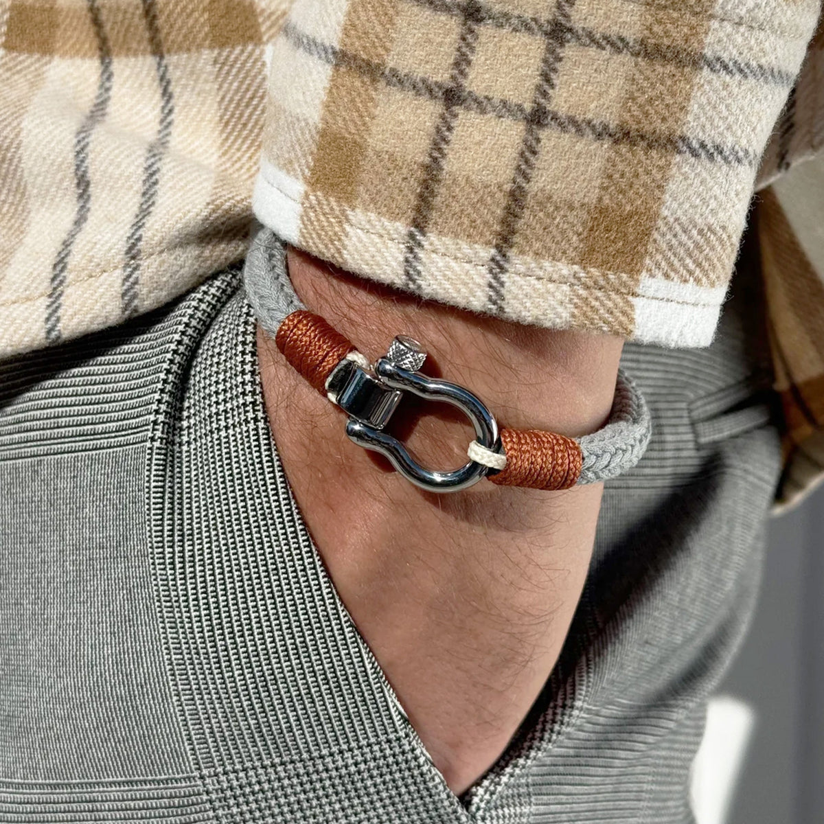Bracelet cordon gris et orange avec mousqueton arrondi en métal argenté porté au poignet.