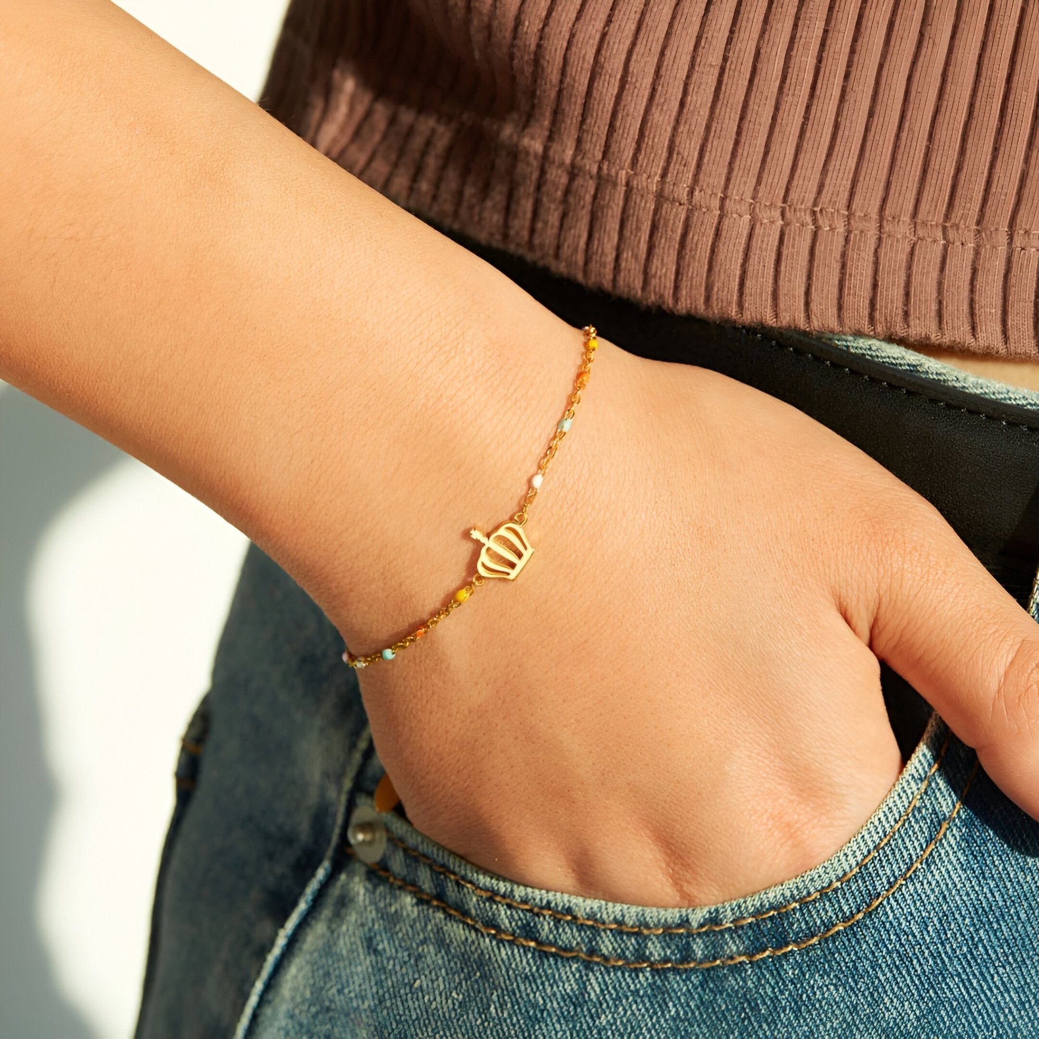 Bracelet fin en or avec pendentif couronne minimaliste sur poignet féminin.