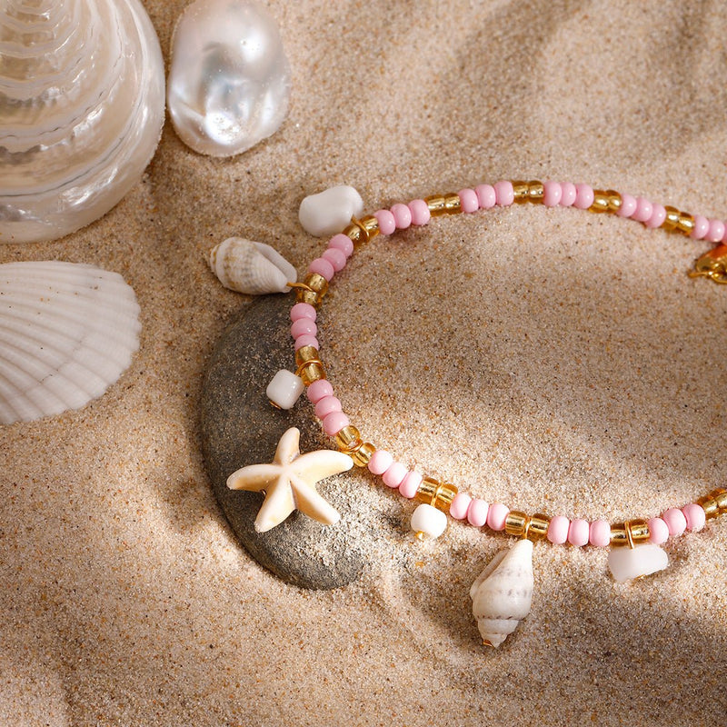 Bracelet de cheville rose en perles avec étoile de mer blanche en résine sur du sable fin.