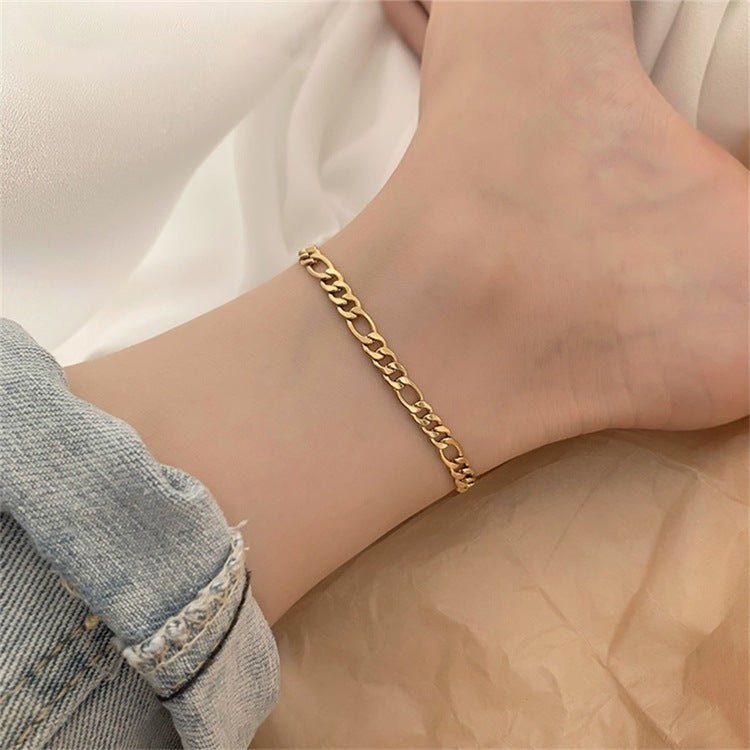 Bracelet de cheville en acier inoxydable doré, maille figaro fine, porté sur cheville féminine.