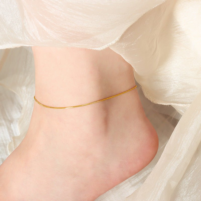 Bracelet de cheville fin en acier inoxydable doré à maille serpent élégant sur peau féminine.
